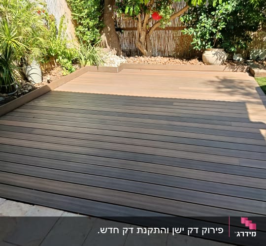 דק עץ בגינה עם צמחים מסביב ועץ גדול ברקע